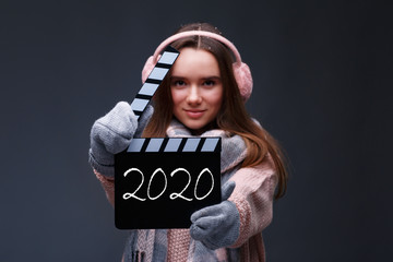 Young beautiful smiling girl in knitting pullover holding director's clapper board for making Christmas video in studio.Movie production clapper board.Lights, camera, action. Start of winter holidays.