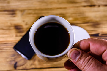 Modern smartphone with blank screen on a wooden background and hand with cup of coffee