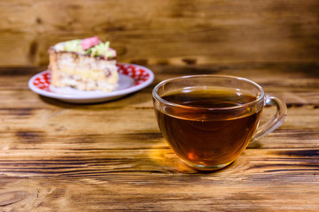 Cup of tea and plate with slice of Kiev cake with cream, nuts and meringue on a wooden table