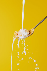 spoon with cornflakes and milk stream with splashes isolated on yellow