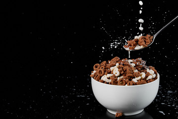 white bowl with assorted cereal and spoon with milk drops isolated on black - Powered by Adobe