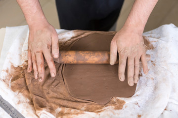 Obraz na płótnie Canvas Pottering Ideas and Concepts. Closeup of Hands of Male Worker Rolling a Piece of Wet Clay on Table Before Moulding.