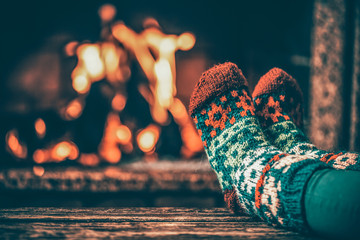 Feet in woollen socks by the fireplace. Woman relaxes by warm fire and warming up her feet in...