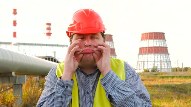 Funny worker, engineer, or electrician mimicking and showing his tongue like a clown in front of a power station