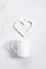 White ceramic cup of hot cocoa on top of white marble background with heart shape marshmallow