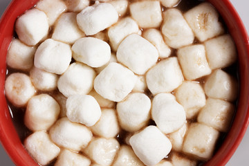 Red ceramic cups of hot cocoa with marshmallows on top of white marble background