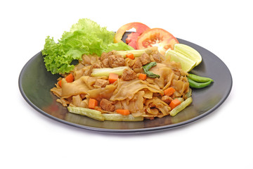 Stir fried flat noodle with black soy sauce, tofu, carrots and green vegetables in black color dish isolated on white background. Thai style stir fry flat noodle. (Pad See Ew) Vegetarian food.
