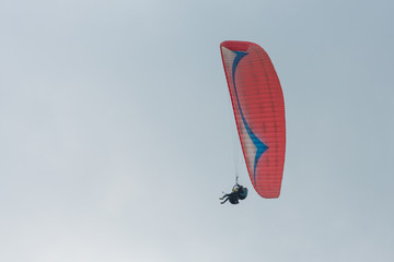 There is a red paraglider flying over the cloudy sky