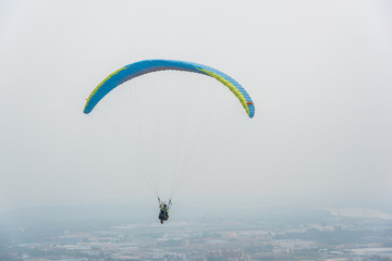 A blue paraglider flying over the plains of the town in gray weather
