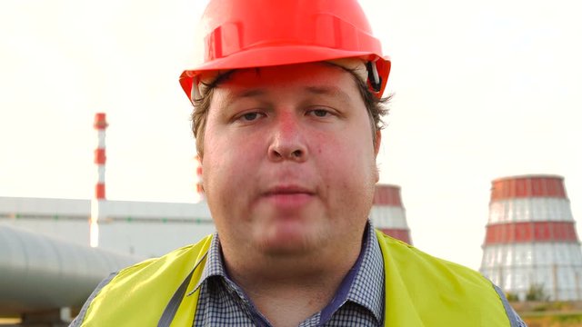 Worker, engineer, or electrician looking directly at the camera reads a tongue twister in front of a power station