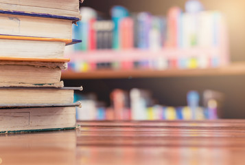 Textbook stack on wooden table with blur background of bookshelf in library with copy space. Photo concept of education, knowledge, traditional learning, and literature. Selective Focus