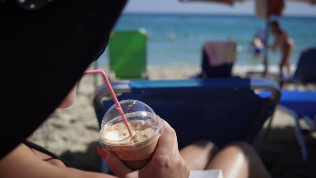 Curly hair female reading a book and refresh drinking frape coffee on the beach