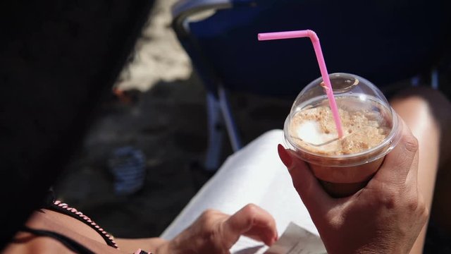 Portrait of smiling woman relaxing on the beach drinking frappe caffee and reading a book while on summer vacation