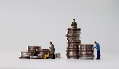 Miniature people carrying coins in a cart and a miniature man sitting on a coin.