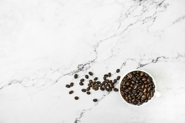 Brown coffee beans with coffee on a marble background with copy space on top of the image.