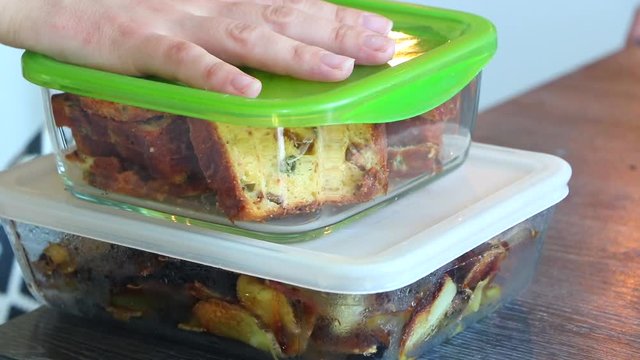 Lunch box with cake and potatoes dish. Tasty organic food. Healthy homemade diet. Delicious pieces of bakery cake in green and glass box. Cold recipe. Closeup on woman's hand and fresh cooking meal. 