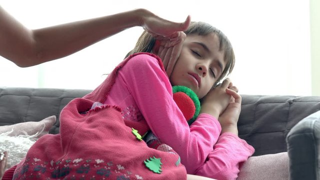 4K Medium shot of adorable little girl sick and sleeping on sofa with mother hand taking temperature on daughter forehead. Mother checking temperature of little child daughter illness with fever.