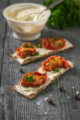 A jar of cream cheese and toast with sun-dried tomatoes on a wooden table.