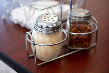 A set of parmesan cheese and crushed red pepper flakes shakers on a wooden table, in a restaurant setting.