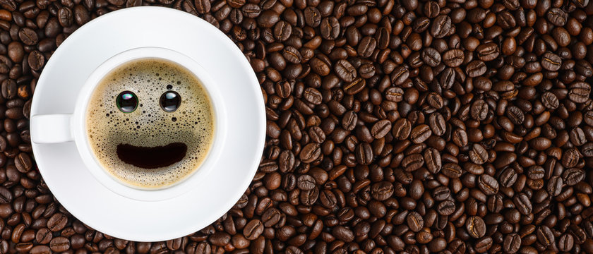 panoramic coffee background of a cup of black coffee with smiling face coffee bubble on background of roasted arabica coffee beans