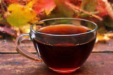 glass Cup of hot tea on wooden planks on background wet window glass from drop of rain behind which lies a pile of bright red yellow autumn fallen leaves
