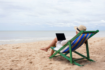 A woman using and typing on laptop computer while lying down on a beach chair