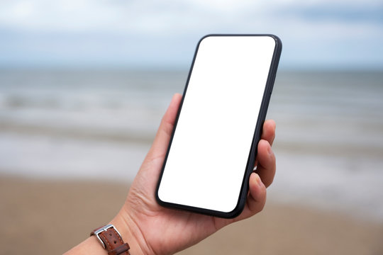 Mockup image of hands holding black mobile phone with blank desktop screen by the sea