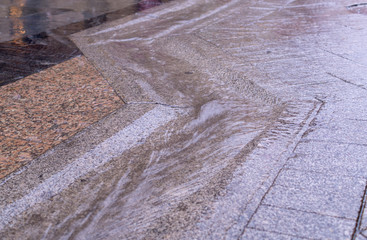 urban street gutter with water flow on tiled sidewalk at rainy day. background, weather.