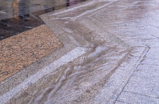 urban street gutter with water flow on tiled sidewalk at rainy day. background, weather.