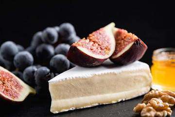 Camembert or brie cheese slice with figs, black grapes, honey and walnuts on black background