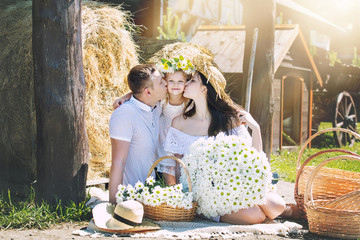 Beautiful happy family father, mother and sweet little daughter together with bouquet of flowers, portrait on hay background on rural farm