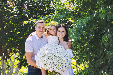 Beautiful happy family father, mother and cute little daughter together with a bouquet of flowers, portrait in the Park