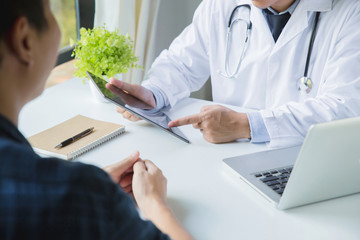 Doctor consulting with male patient, presenting results on tablet computer, sitting at desk.