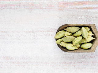 Spice Green cardamom (Elettaria cardamomum) in a scoop on a white wooden background with copy space