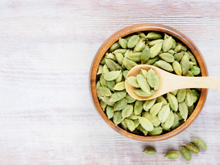 Spice Green cardamom (Elettaria cardamomum) in a wooden cup and spoon vertically on a white wooden background