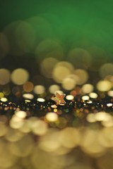 Festive bokeh background.Star and gold glitter with  bokeh on a black-green blurred background.Christmas and New Year background.Winter holidays wallpaper.