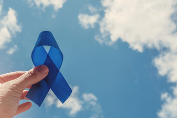 Hand holding blue ribbon on blue sky background , Prostate Cancer Awareness, Movember Men health...