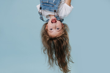 beautiful little girl hanging upside down on blue background