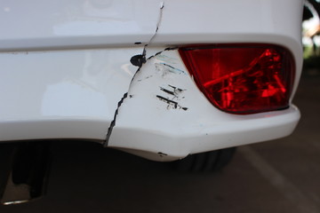 The rear bumper of a white car has cracks due to an accident on the road