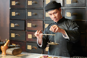 Concentrated tradiotional Asian medicine practitioner weighting herbs and roots on old scales