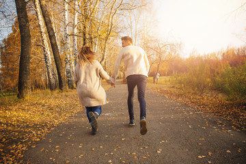 Fototapeta premium Happy couple in love runs through autumn forest, man smile throws maple yellow leaves