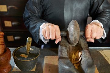 Hands of Asian traditional medicine practitioner grinding up dry herbs and roots in special boat...