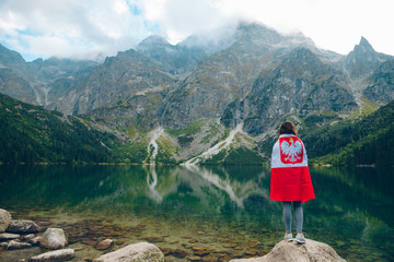 young woman covered with poland flag looking at lake in tatra mountains