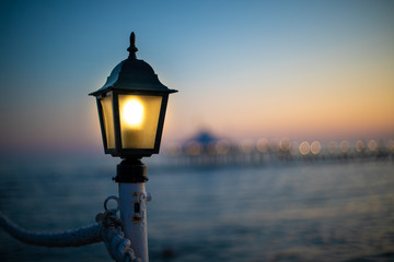 a lantern on a bathing jetty glows bright yellow at dusk