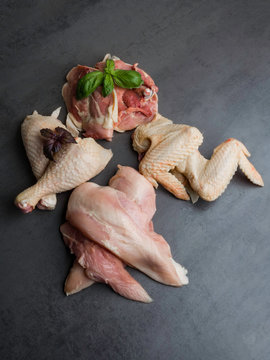 Fresh raw chicken parts on grey background. Breast, wings and legs, fillet with basil leaf, selective focus
