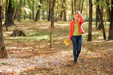 Naklejka na ściany i meble young woman collects fallen leaves in a city park. Autumn weather, golden leaves.