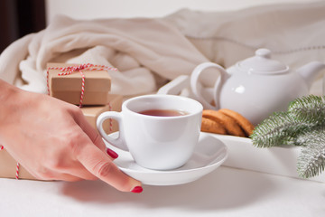 Woman put a cup of tea nearby gift boxes, tray with teapot and cookies.