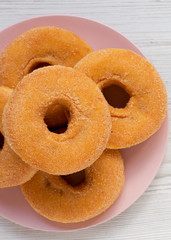 Homemade apple donuts ready to eat on a pink plate on a white wooden surface. From above, overhead, flat lay.