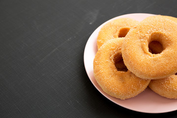Homemade autumn apple-cinnamon donuts on a pink plate on a black surface, side view. Copy space.