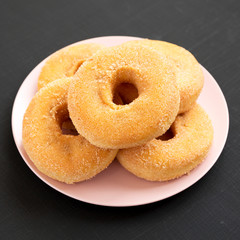 Homemade autumn apple-cinnamon donuts on a pink plate on a black background, side view. Close-up.
